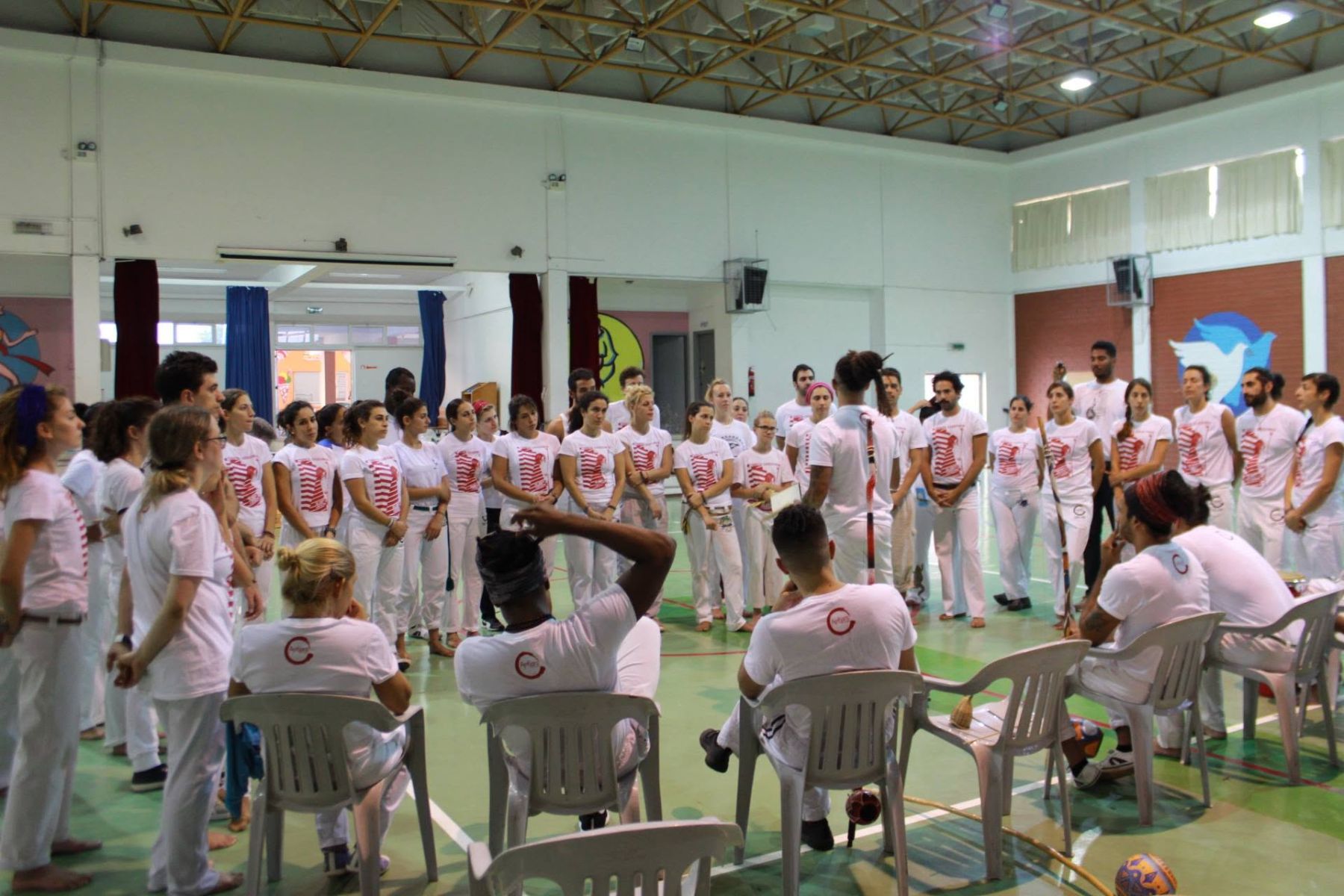 Capoeiristas in white standing in a large circle in a sports hall during the 30 Years Celebration