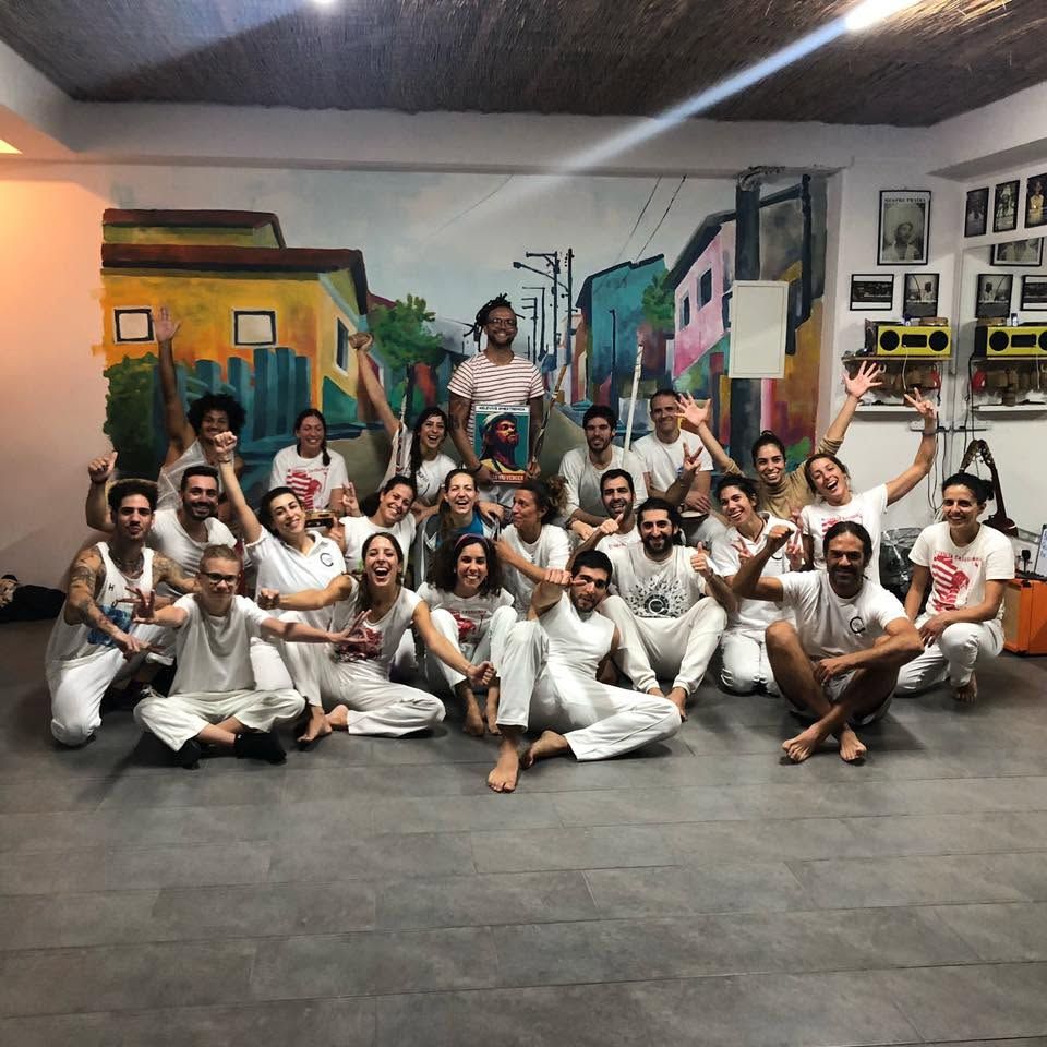 Apêiara students at the academy holding a portrait of Mestre Moa do Katendê during a tribute roda